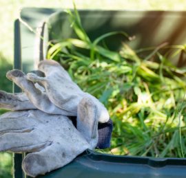 Green bin container filled with garden waste. Dirty gardening gloves. Spring clean up in the garden. Recycling garbage for a better environment