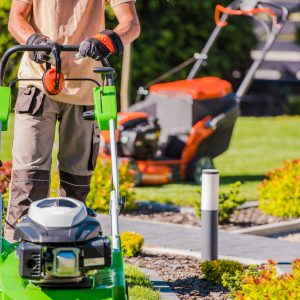 Male Landscaper Doing Garden Maintenance Work with His Professional Equipment Using Two Different Lawn Mowers.